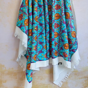 May include: A turquoise tablecloth with a white border and fringe. The tablecloth features a repeating pattern of stylised flowers and leaves in shades of orange, red, purple, and white.