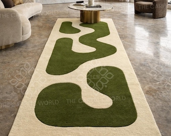 Puede incluir: Una alfombra rectangular con un fondo color crema y un gran diseño verde abstracto. La alfombra está colocada en un salón moderno, con un sofá, una mesa de centro y un sillón visibles. El diseño presenta formas interconectadas.