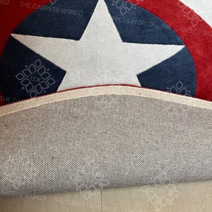 May include: A close-up of a red, white, and blue Captain America themed rug with a white star in the center. The rug is rolled up and the underside is visible.