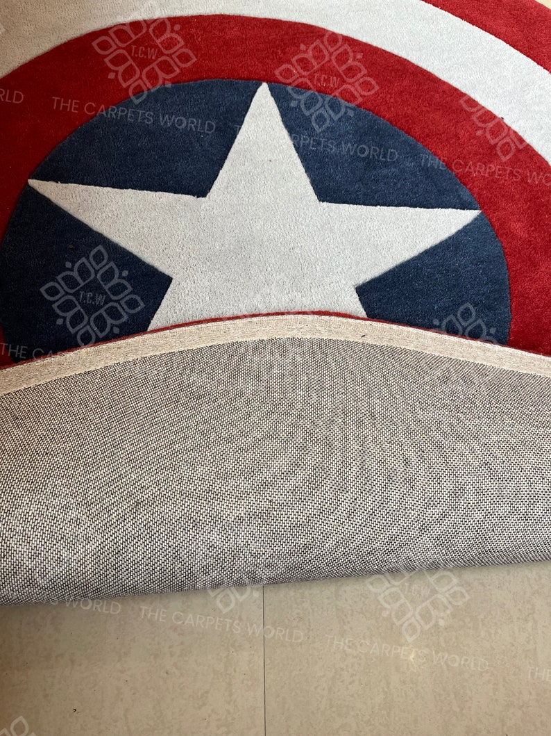 May include: A close-up of a red, white, and blue Captain America themed rug with a white star in the center. The rug is rolled up and the underside is visible.