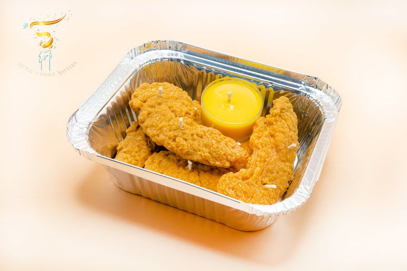 Several chicken tender shaped candles are placed inside a aluminum foil box, together with a yellow tea light which is the mustard sauce here.