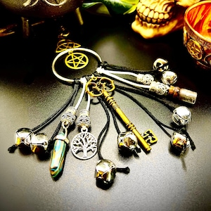 May include: A black and white key charm with a variety of charms, including a tree of life, a key, and bells. The charm is hanging from a black and white cord.