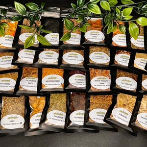 May include: A collection of 40 small, clear plastic bags filled with various dried herbs and spices. Each bag has a white oval label with black text that reads "The Apothecary Witch" and the name of the herb or spice.
