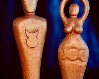 May include: Two gold-colored wooden statues, one with antlers and a crescent moon symbol, the other with a triple moon symbol and arms raised above the head.