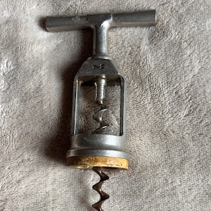 Könnte beinhalten: Ein Vintage-Korkenzieher aus Metall mit einem T-förmigen Griff und einer Wendel. Der Korkenzieher hat eine silberne Oberfläche mit einem Holzsockel. Das Design ist einfach und funktional, geeignet zum Öffnen von Weinflaschen.