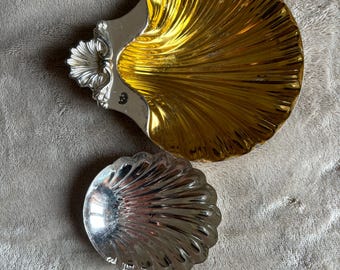 Könnte beinhalten: Zwei silberne Schalen in Muschelform, eine davon mit goldener Oberfläche. Die größere Schale hat einen dekorativen Griff.