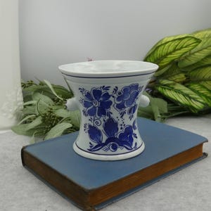 May include: A white ceramic vase with blue and white floral designs. The vase has two small handles on the sides and a flared top.