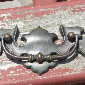 May include: A decorative metal drawer pull with a leaf design. The pull is a dark bronze color and has a curved handle.