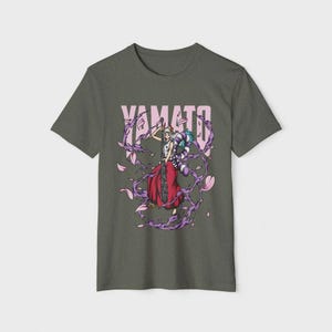 Op de afbeelding: Donkergrijs t-shirt met een afbeelding van een personage in een rode rok met een zwaard. De roze tekst "YAMATO" staat boven het personage. Paarse en roze bloemaccenten omringen het personage.