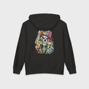 Op de afbeelding: Zwarte hoodie met ritssluiting met een kleurrijke schedelafbeelding op de rug. De schedel draagt een rode bandana en houdt een pistool vast, met ringen aan de vingers. Het ontwerp heeft een gedurfde, illustratieve stijl.