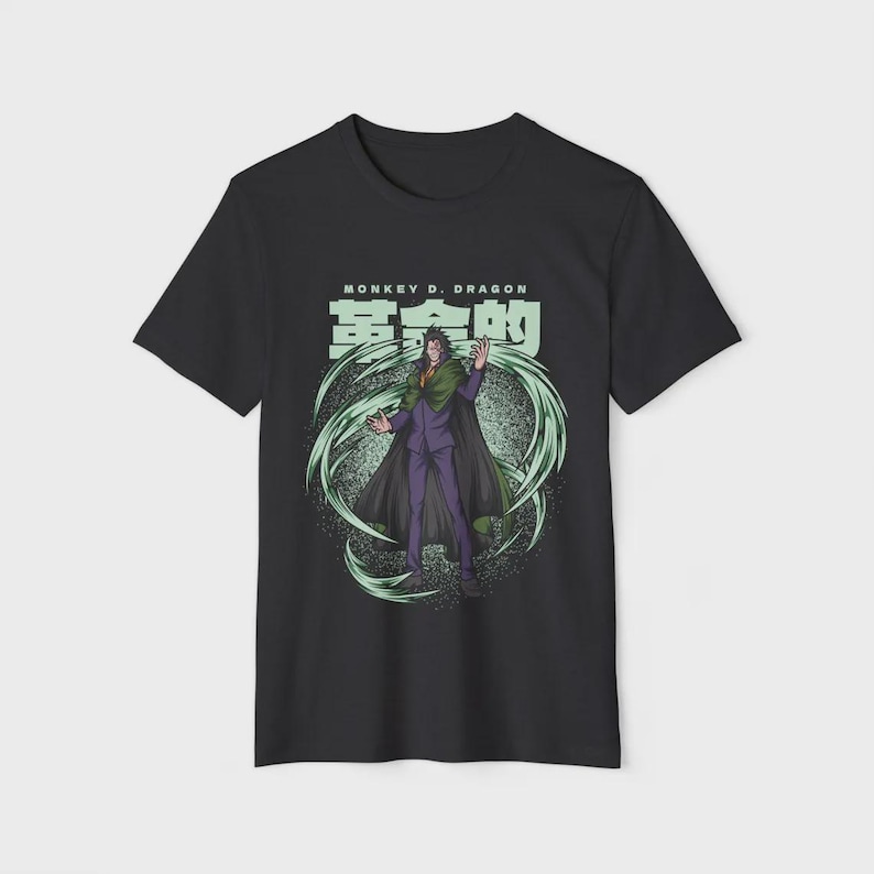 Op de afbeelding: Zwart t-shirt met een afbeelding van een personage in een paars pak en groene cape, omringd door groene energie wervelingen. De tekst "MONKEY D. DRAGON" en Japanse karakters staan boven het personage.