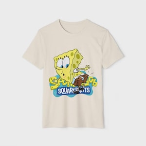 Op de afbeelding: Cr&egrave;mekleurig T-shirt met een cartoonafbeelding van SpongeBob SquarePants. Het gele personage wordt afgebeeld met een verbaasde uitdrukking, naast de woorden "SQUAREPANTS" in een blauw en geel ontwerp.