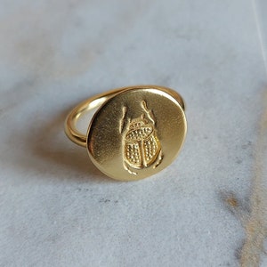Anillo de sello con forma de escarabajo redondo con un escarabajo grabado en la superficie. Anillo tipo sello de plata bañada en oro amarillo con un escarabajo. Anillo de escarabajo hecho a mano.