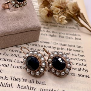 May include: A pair of antique gold earrings with black gemstones surrounded by a circle of pearls.