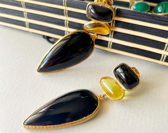 May include: A pair of dangle earrings featuring black and yellow stones. The earrings are made of gold metal and have a teardrop shape.