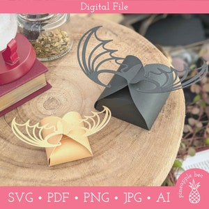 May include: Two bat-shaped favor boxes, one black and one brown, with intricate cut-out designs. The boxes are sitting on a wooden surface.