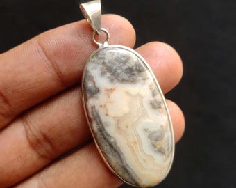May include: Oval pendant with a silver bail. The pendant features a polished stone with a swirling pattern of gray, cream, and white colors. The stone is set in a silver bezel.
