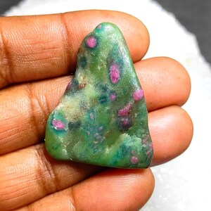 Può includere: Una gemma naturale di forma irregolare, con una base verde e inclusioni rosa e rosse. La pietra è tenuta in mano, evidenziando la sua consistenza unica e le variazioni di colore. Un'opera d'arte naturale unica.