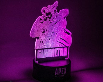 May include: A purple and white 3D printed acrylic lamp with a silhouette of the character Gibraltar from the video game Apex Legends. The lamp base is black and has the Apex Legends logo.