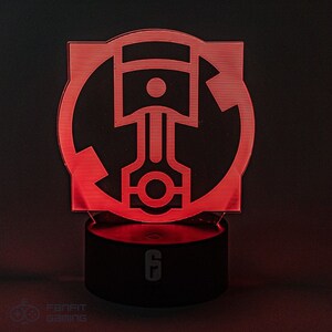 May include: Red LED light with a black base. The light features a circular design with a piston and arrow graphic. The base has the number "6" printed on it.