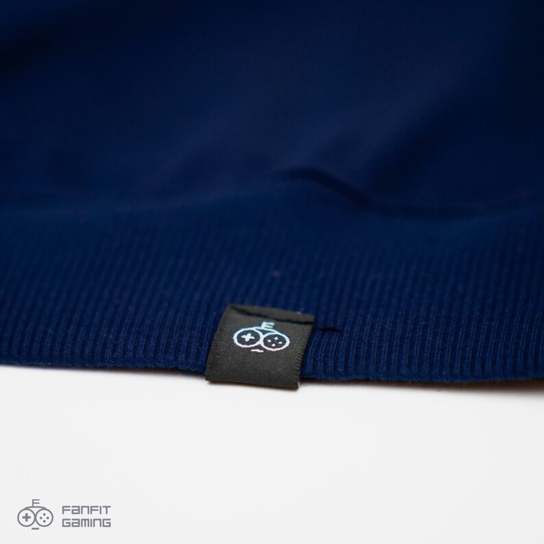 May include: Close-up of a navy blue sweatshirt with a black label featuring a white logo of two video game controllers.