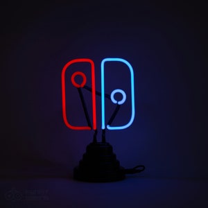 May include: A neon sign shaped like the Nintendo Switch logo. The left side is red and the right side is blue. The sign is on a black base.