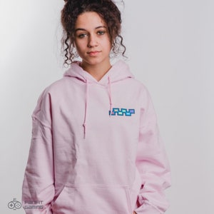 May include: A pink hoodie with a colorful pixelated logo on the front. The logo is a series of squares in different colors, including blue, green, yellow, and pink.