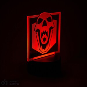 May include: A red illuminated acrylic light with a black skull design. The skull has a large open mouth with a gear inside. The light is on a black base.