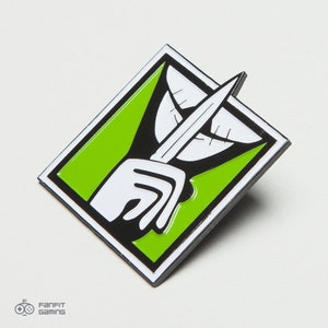 May include: A green and black enamel pin with a white hand holding a finger to its lips, a white mouth with teeth, and a black outline. The pin is shaped like a square with rounded corners.
