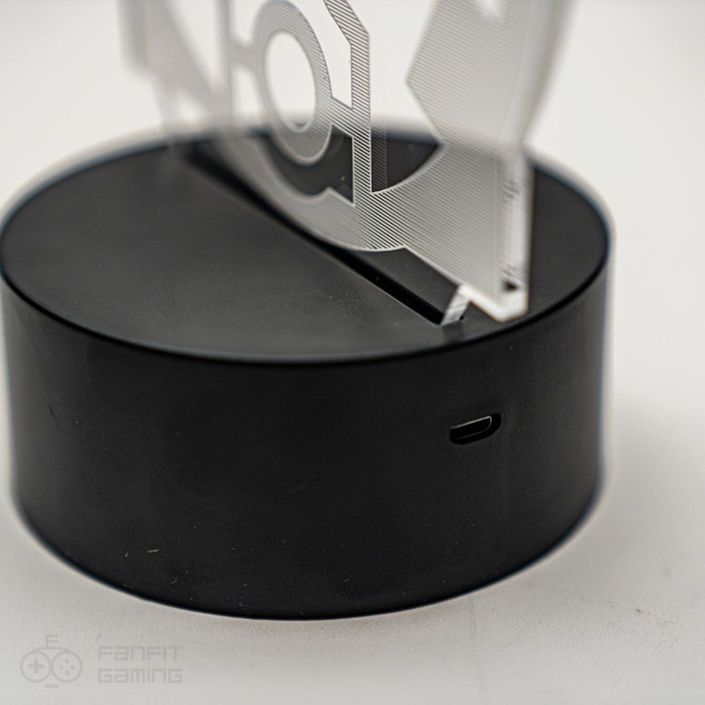 May include: A black circular base with a USB charging port on the side. A clear acrylic figure sits on top of the base.