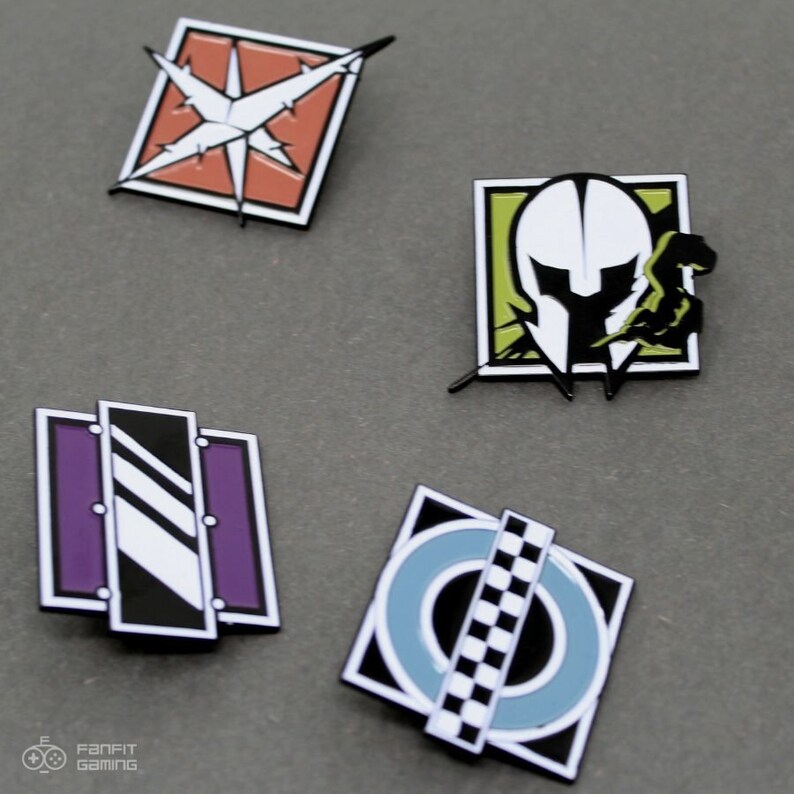 May include: Four enamel pins featuring different designs from the video game Rainbow Six Siege. The pins are square shaped with black outlines and feature a white star with orange background, a white helmet with a green background, a purple and white striped design, and a blue circle with a black and white checkered pattern.
