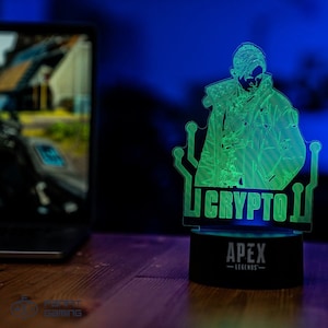 May include: A green LED light with a silhouette of a video game character, Crypto, from Apex Legends. The light has a black base with the words "Apex Legends" printed on it.