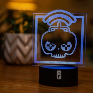 Puede incluir: Un letrero luminoso azul y blanco con un diseño de calavera y huesos cruzados. El letrero tiene forma cuadrada y tiene una base negra con el número "6" en él.