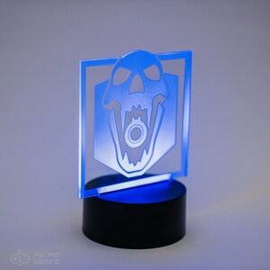 May include: A blue acrylic light-up desk lamp with a white skull design. The skull has a gear in its mouth. The lamp is on a black base.