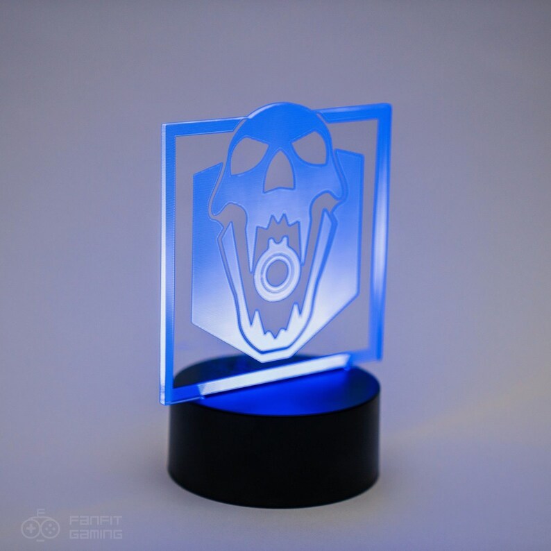 May include: A blue acrylic light-up desk lamp with a white skull design. The skull has a gear in its mouth. The lamp is on a black base.