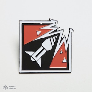 Puede incluir: Pin de esmalte negro y rojo con un diseño de cohete blanco. El cohete está rompiendo una pared roja y blanca agrietada. El pin es de forma cuadrada con un borde blanco.