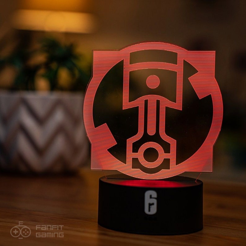 May include: A red illuminated lamp with a black base. The lamp features a stylized image of a piston inside a circle with arrows. The base of the lamp has a white "6" on it.