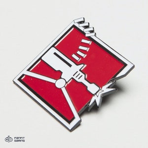 May include: A red and white enamel pin featuring a stylized image of a breaching charge, a common tool used in the video game Rainbow Six Siege.