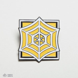 May include: A yellow and white enamel pin featuring a stylized spider web design. The pin is square shaped and has a black outline.