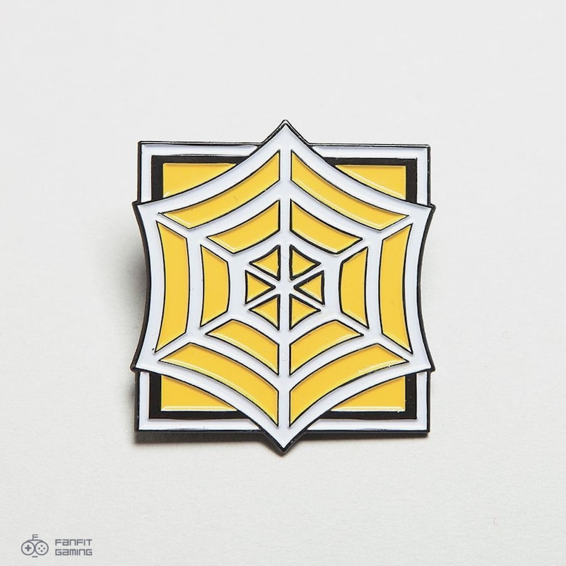 May include: A yellow and white enamel pin featuring a stylized spider web design. The pin is square shaped and has a black outline.