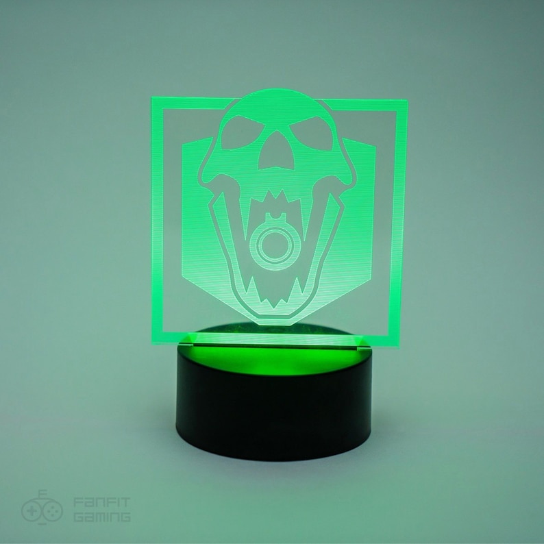 May include: Green acrylic night light featuring a skull and crossbones design. The skull is white and has a gun inside the mouth. The light sits on a black base.
