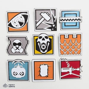 May include: Nine enamel pins featuring different designs from the video game Rainbow Six Siege. The pins are square and have a white border. The designs include a skull, a hammer, a castle, a gas mask, a drone, a wall, and a gun.