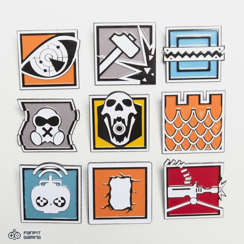 May include: Nine enamel pins featuring different designs from the video game Rainbow Six Siege. The pins are square and have a white border. The designs include a skull, a hammer, a castle, a gas mask, a drone, a wall, and a gun.