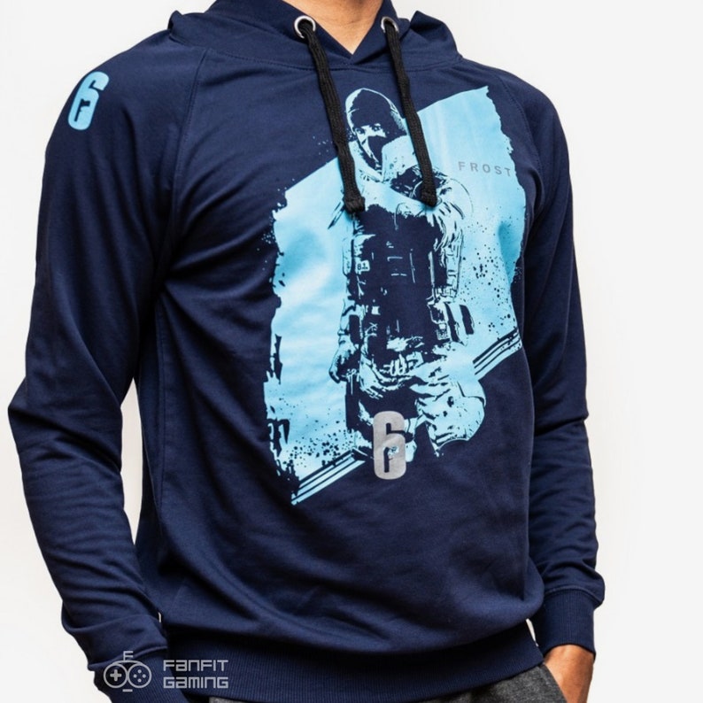 May include: A navy blue hooded sweatshirt with a graphic print of a video game character holding a gun. The character is in front of a blue and white background. The text "Frost" and "6" are printed on the sweatshirt.