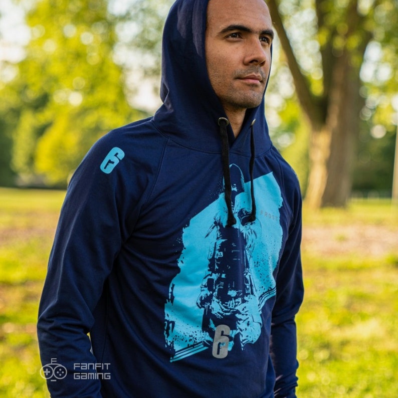 May include: A navy blue hooded sweatshirt with a blue and white graphic print of a person wearing a tactical helmet and holding a gun. The text "Frost" is visible on the graphic. The number "6" is also visible on the graphic.
