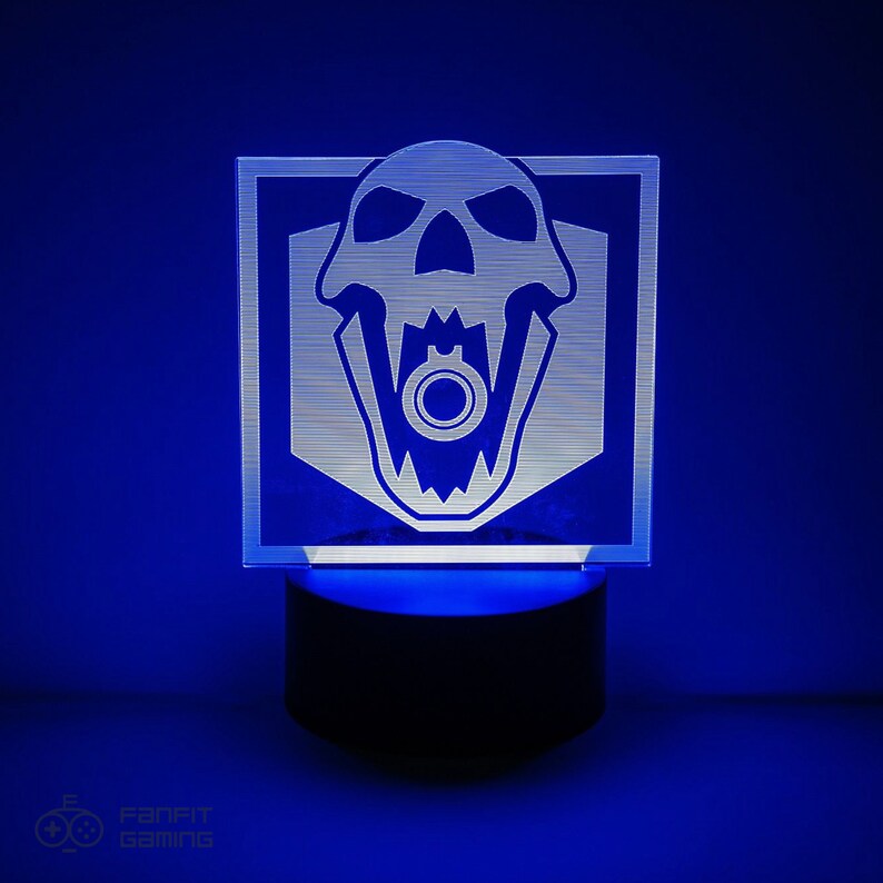 May include: A white acrylic night light featuring a skull design with a gun in its mouth. The light sits on a black base and is illuminated with blue light.