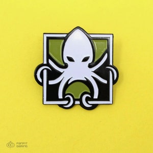 May include: A black and white enamel pin featuring a white octopus with green accents inside a black square with a white border.