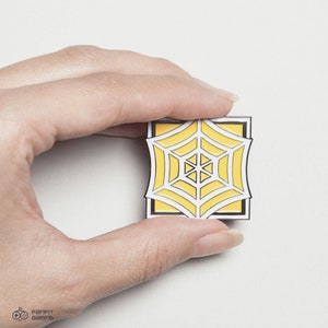 May include: A yellow and white enamel pin featuring a spider web design. The pin is square shaped and has a black outline.