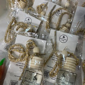 May include: A set of car air fresheners with a gold and white string. The air fresheners are in clear glass bottles with a wooden stopper and a label that says "Sparked Creations Blue Agava & Cacao".