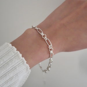May include: A silver chain bracelet with oval links. The bracelet is on a person's wrist.